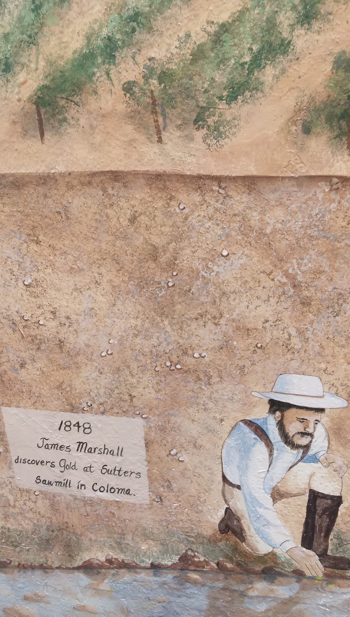Wall with a painting of kneeling man and text that reads, "1848 James Marshall discovers Gold at Gutters..."